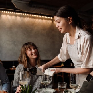 Frau mit Weinkurs schenkt in Restaurant professionell Wein ein